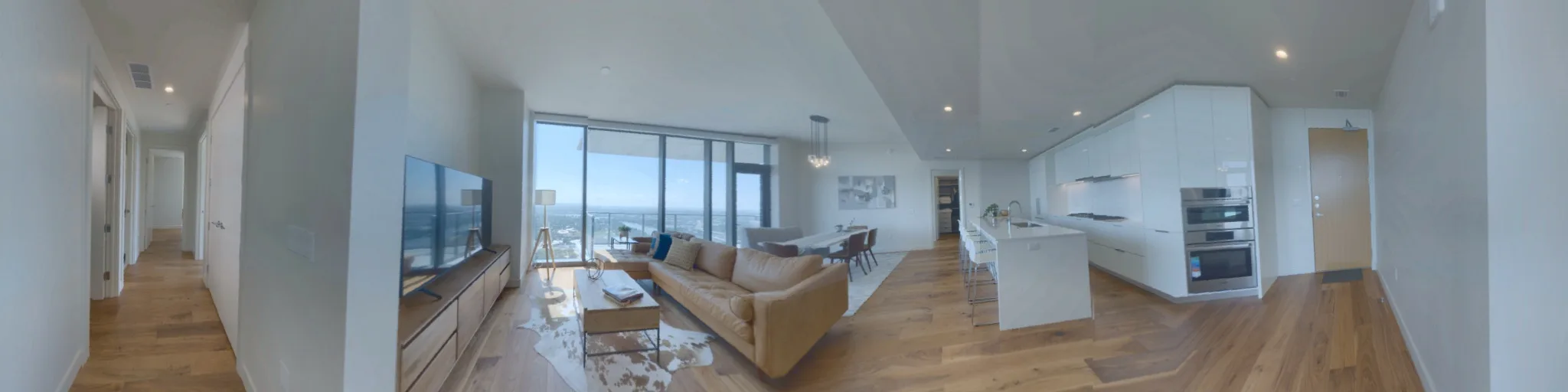 Panorama of the open living room, dining area and white kitchen with a waterfall island, in front of floor-to-ceiling windows